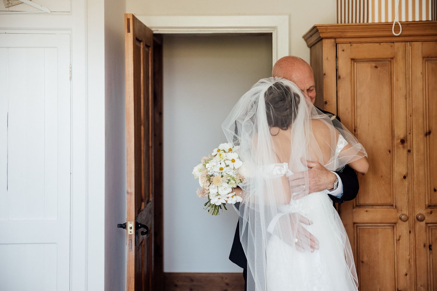 Getting ready moments captured in a bright room with wooden doors and natural light.