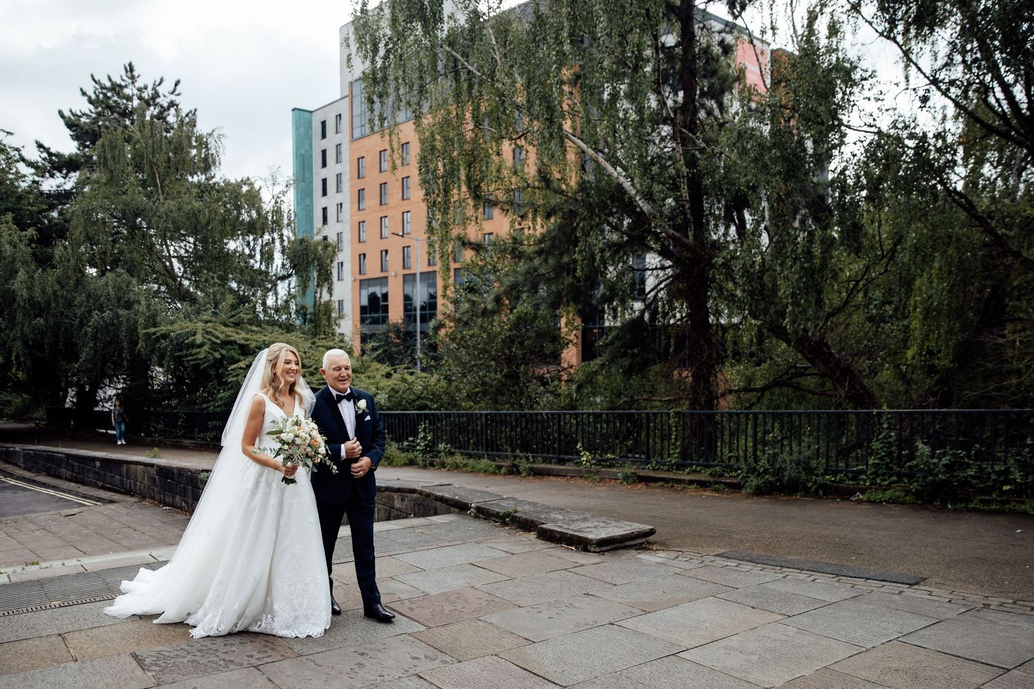 Newlyweds walking together on urban pathway surrounded by trees.