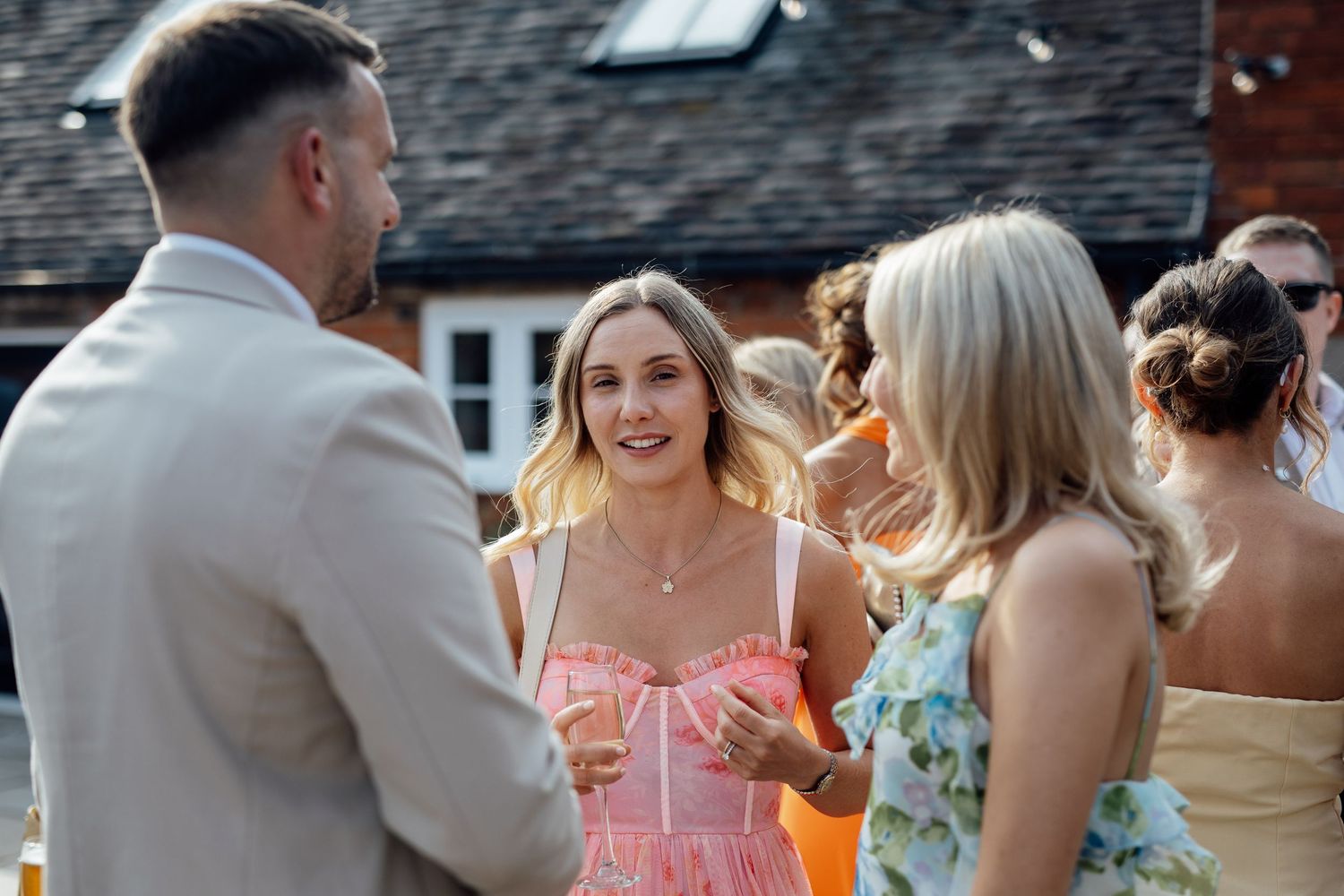 Wedding guests mingle and celebrate during an outdoor reception against a rustic brick backdrop.