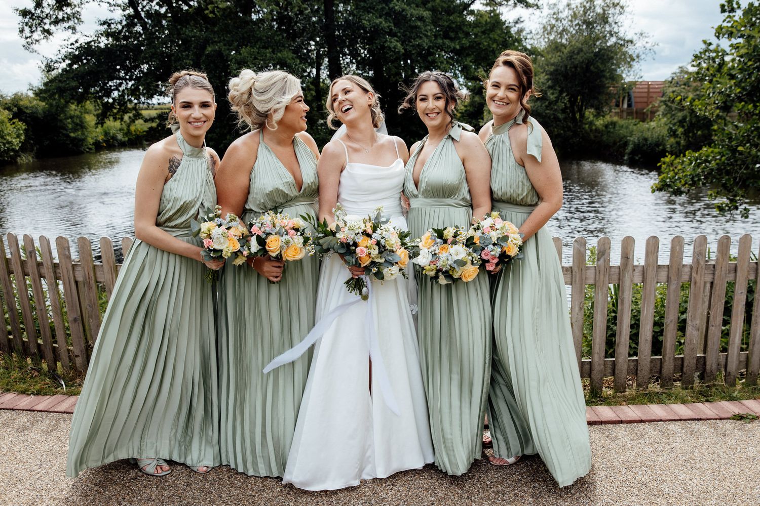 Bridesmaids in sage green dresses pose with the bride in a garden setting.