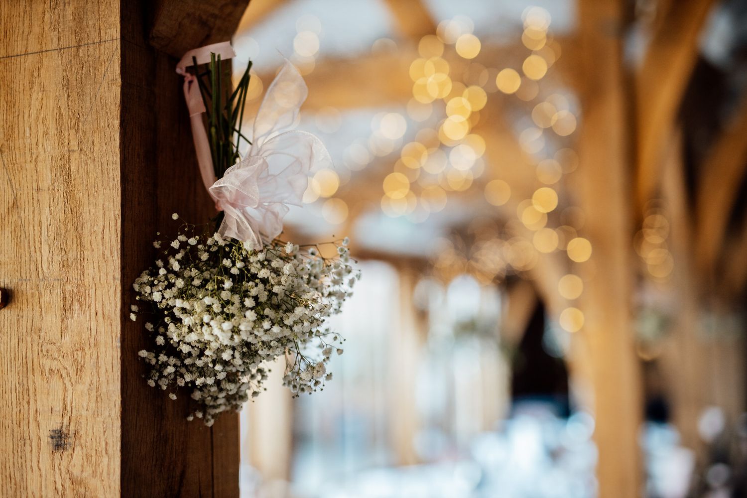 Baby's breath and floral decorations hanging against wooden beam with bokeh lights.