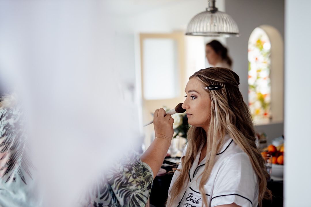 A woman in white getting her makeup done during wedding preparations.