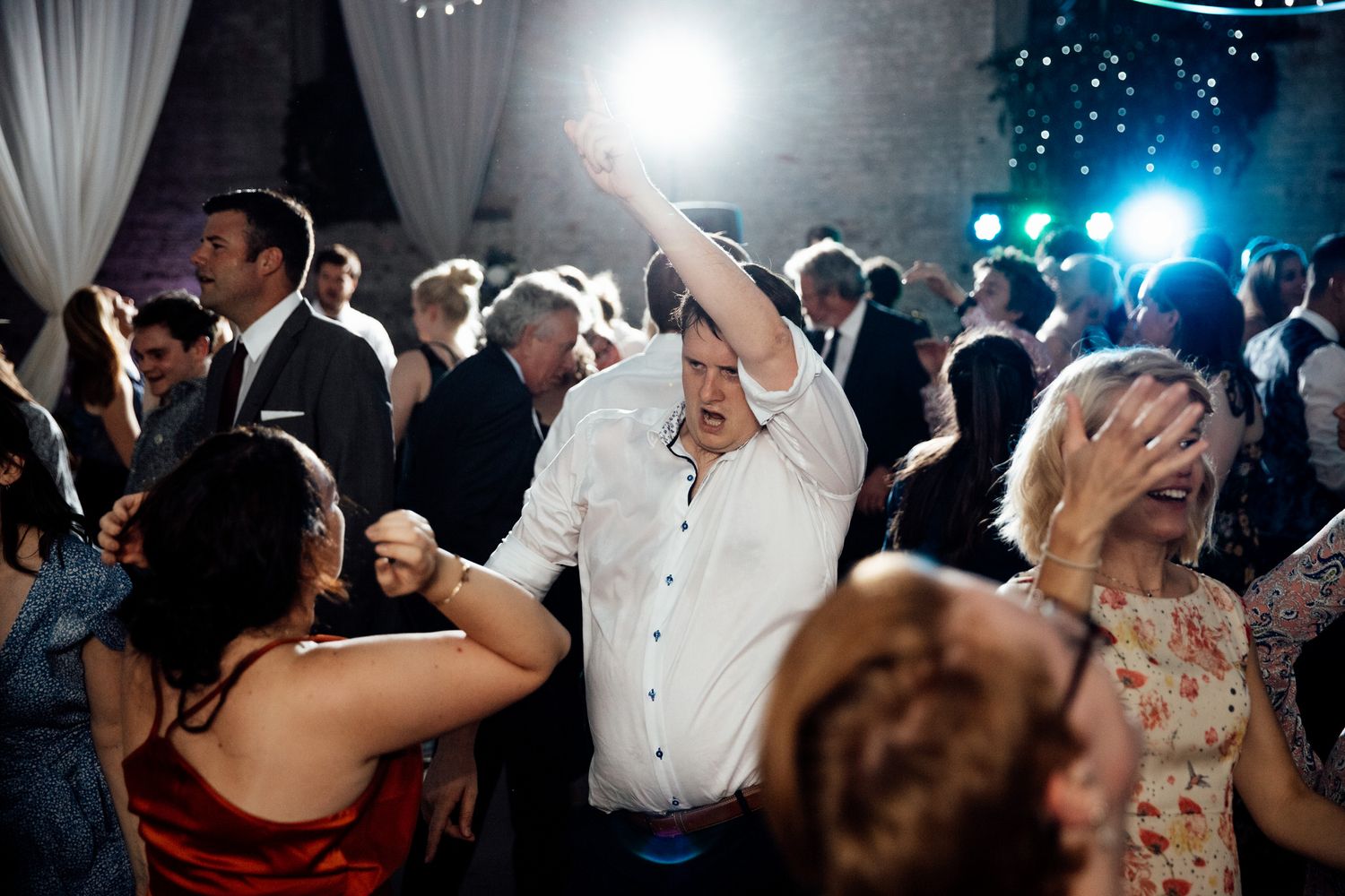 Energetic dance party scene with guests celebrating on the dance floor under colorful lights.