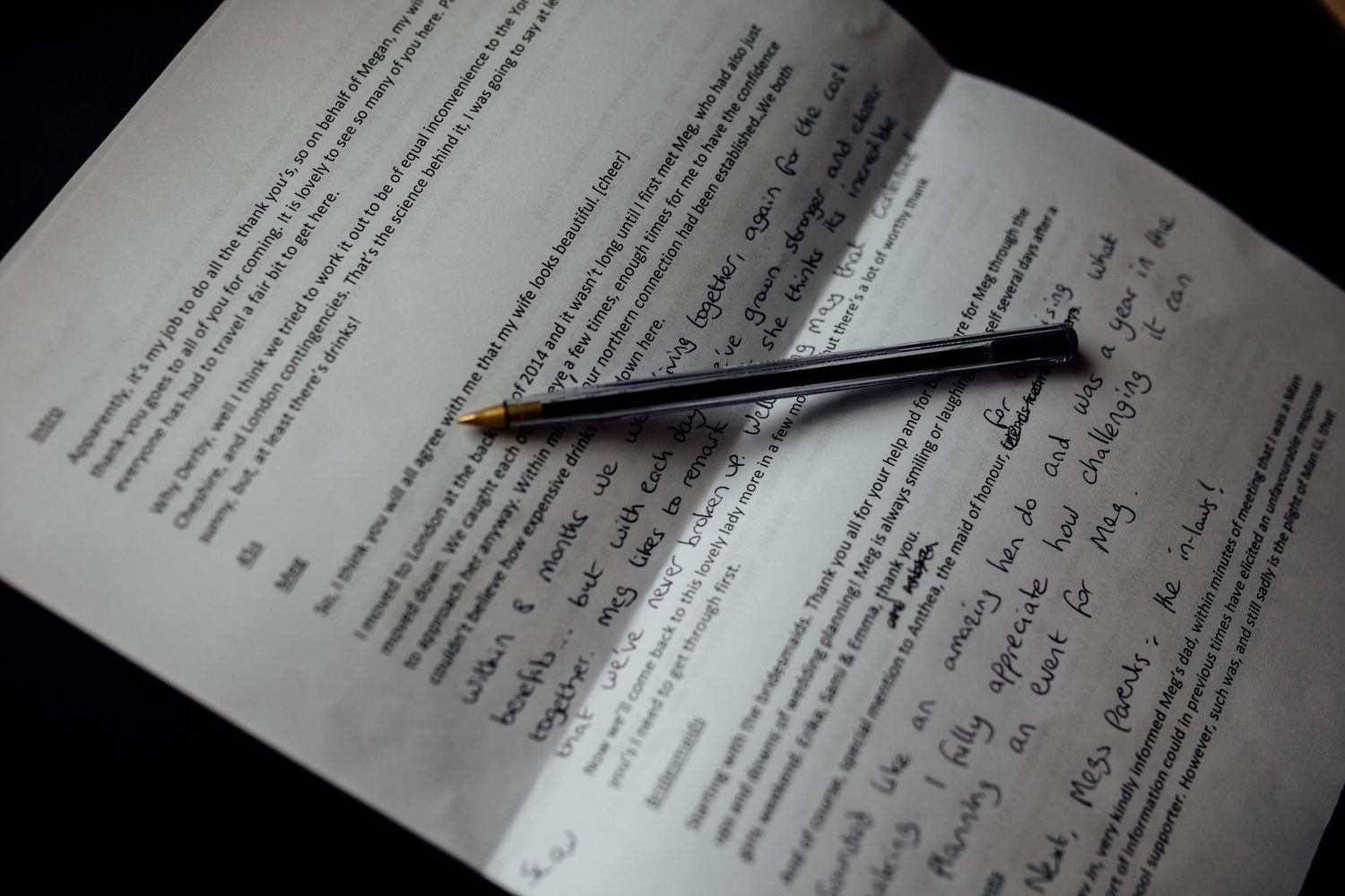 Close-up of wedding document being signed with black pen on white paper.