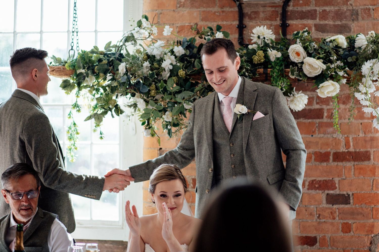 Wedding reception decor featuring white floral arrangements against exposed brick walls.