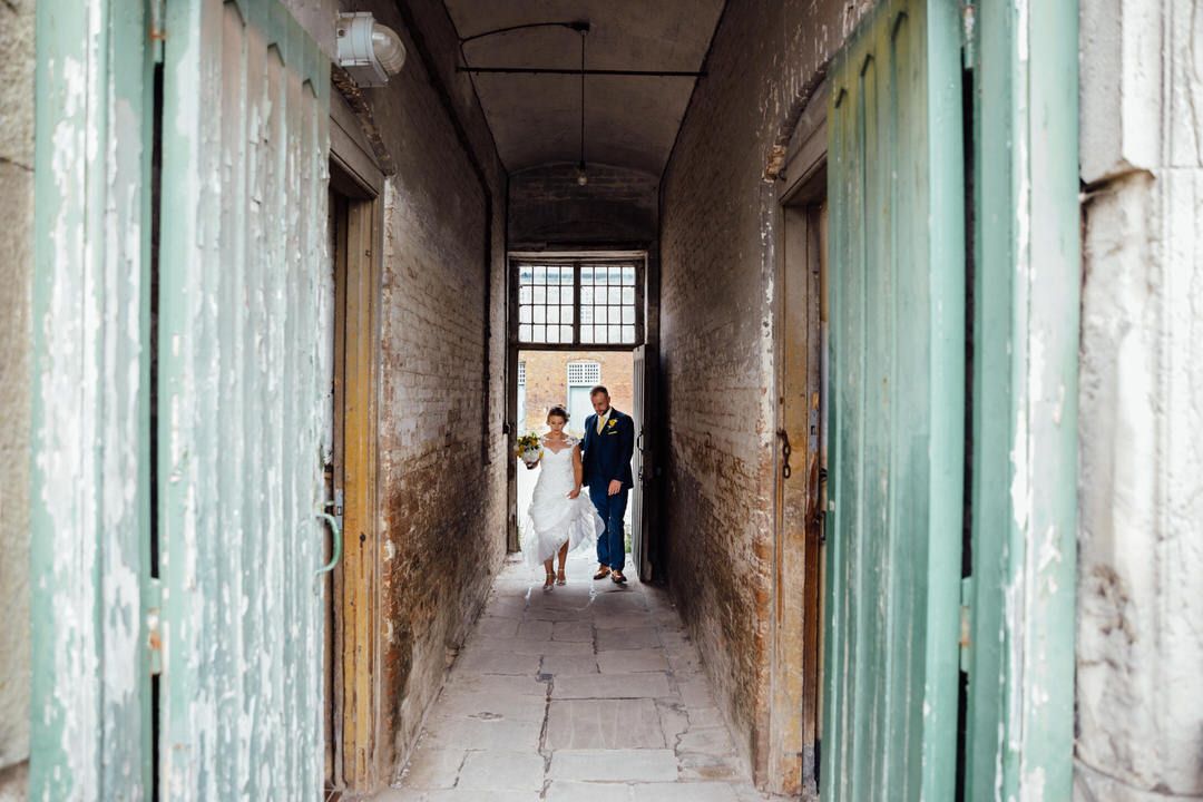 A couple walks through an industrial hallway with mint green doors and exposed brick walls.