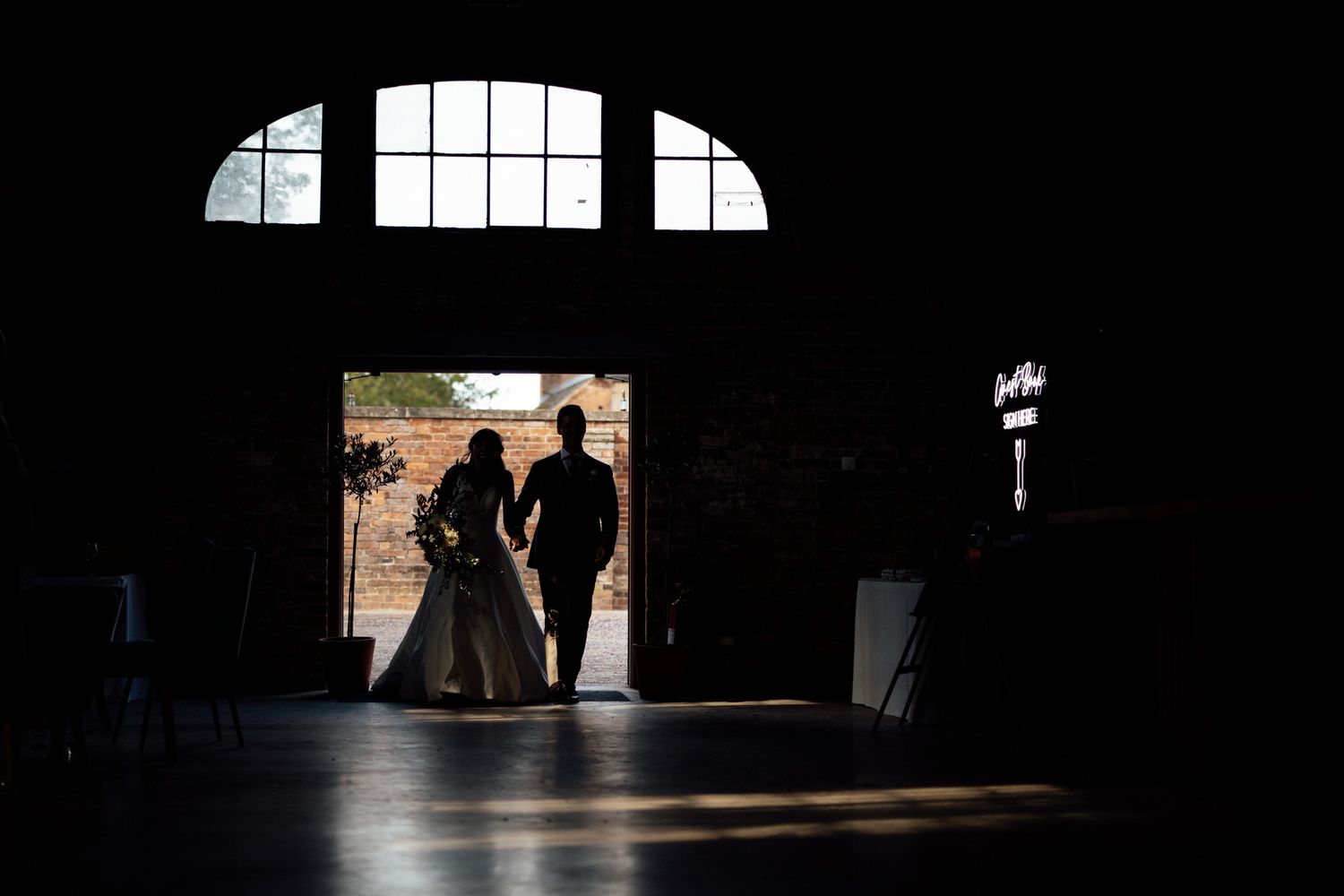 Silhouettes against arched windows create dramatic composition in dark venue.