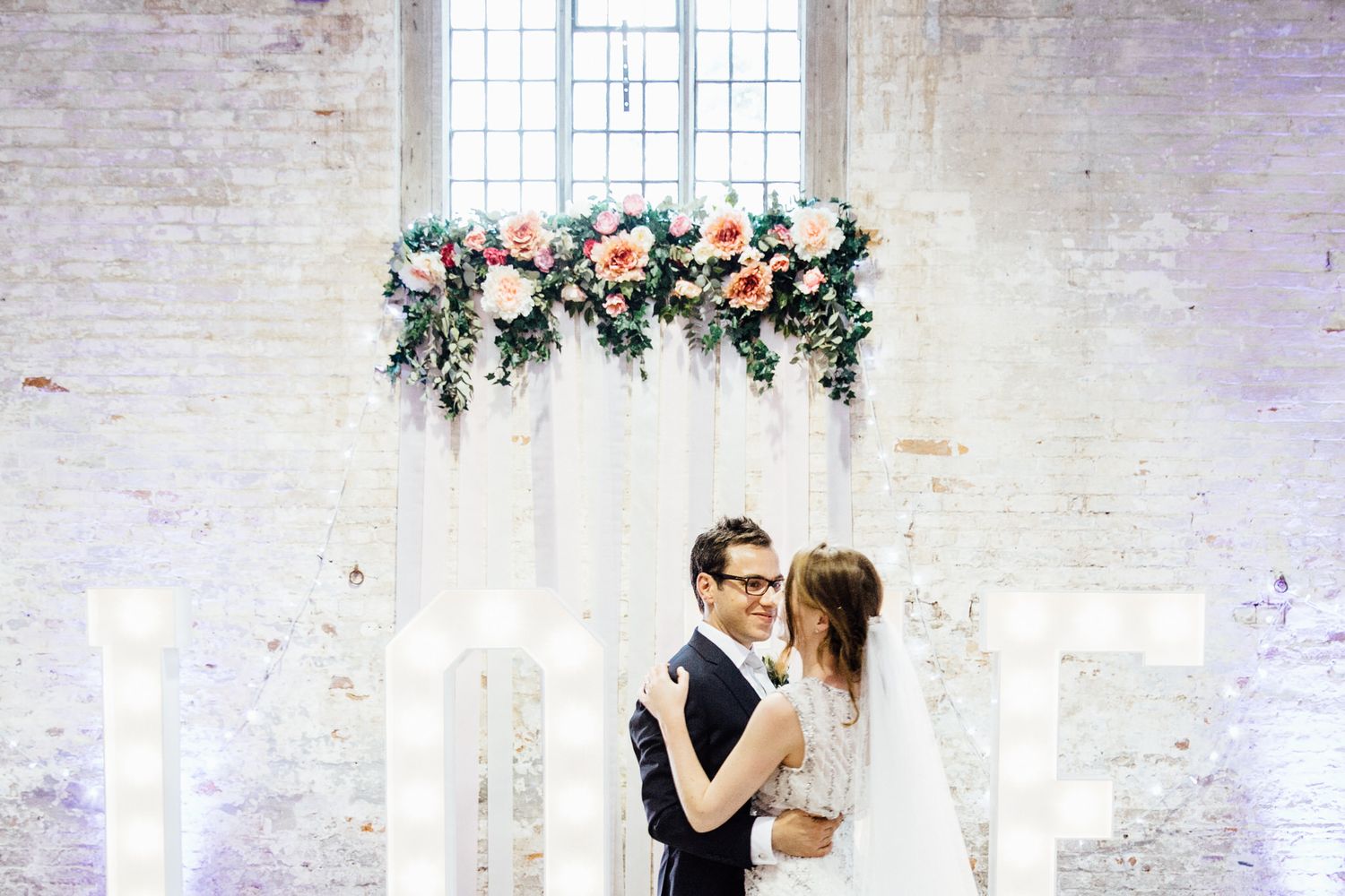 Couple sharing a romantic dance moment under floral decorations in a rustic brick venue.