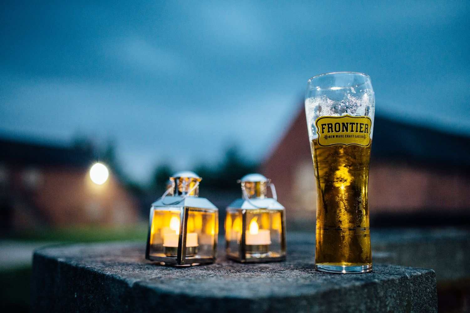 Glass of beer and lanterns at dusk during outdoor wedding reception.