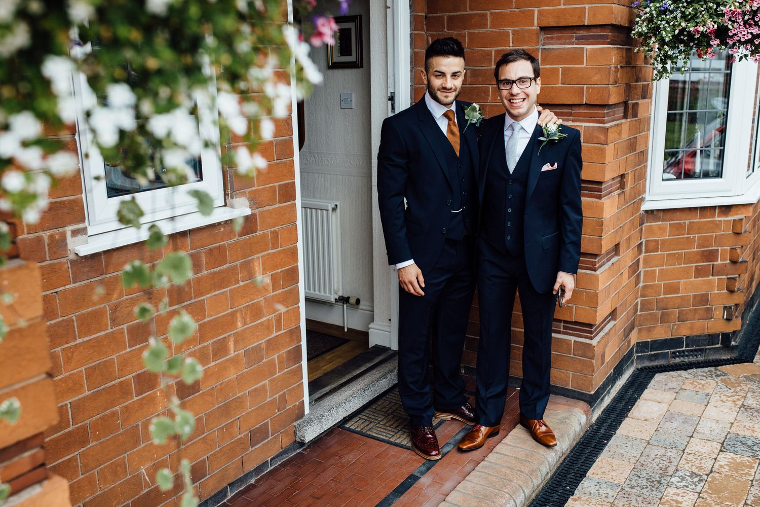 Wedding party members pose in formal attire against a brick building exterior.