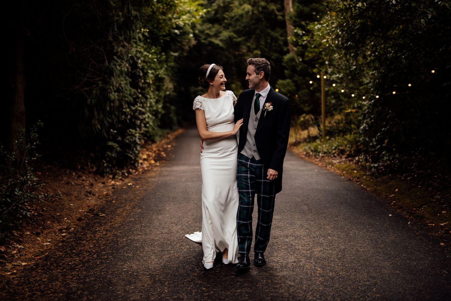 A romantic wedding couple walks along a tree-lined path during an autumn photoshoot.