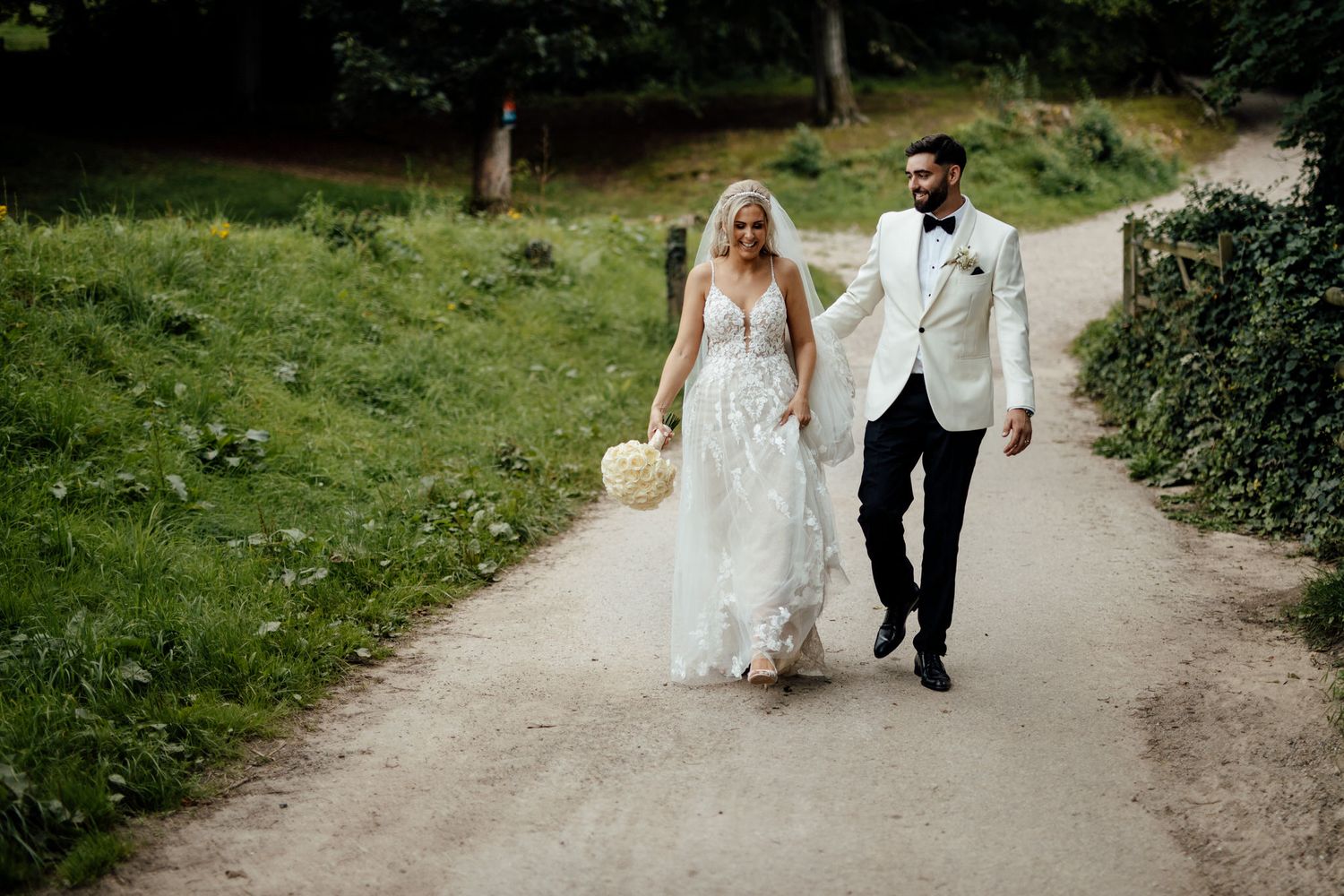 Wedding party walking along tree-lined path in natural outdoor setting.