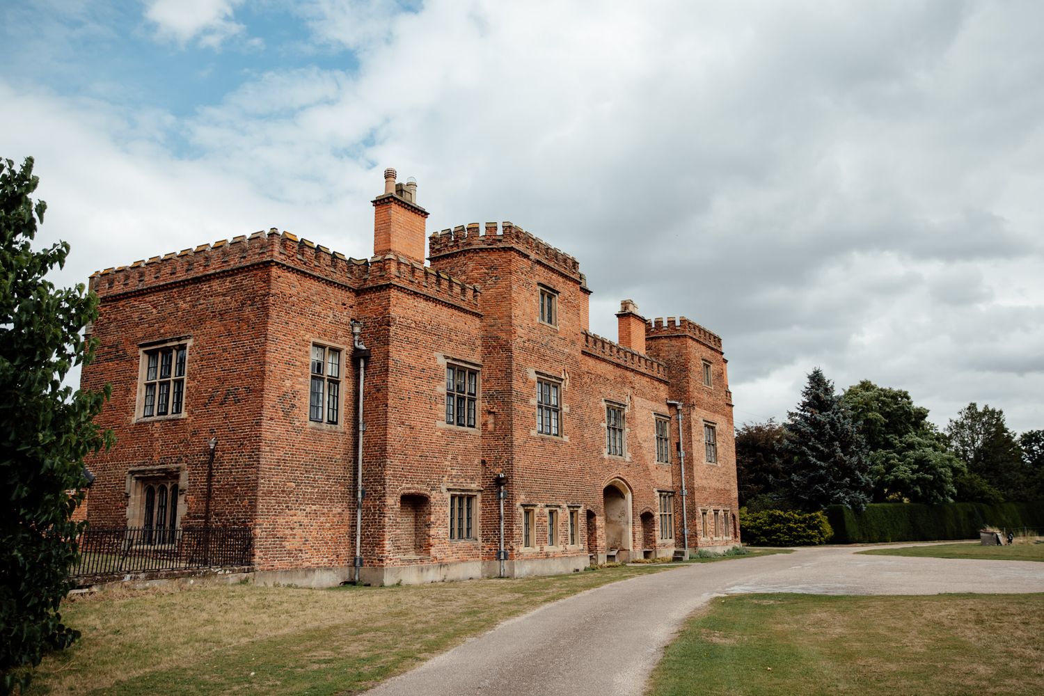 Panoramic view of a historic brick castle venue with beautiful landscaping on a cloudy day.