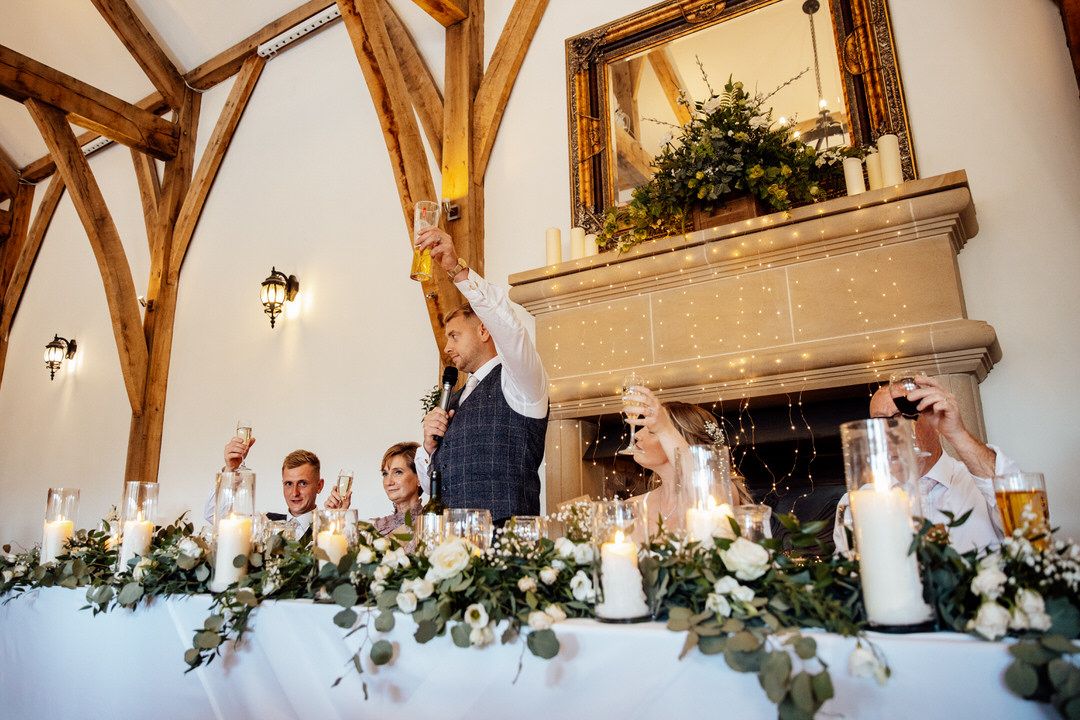 Interior of elegant wedding venue with exposed wooden beams and white walls decorated with greenery.