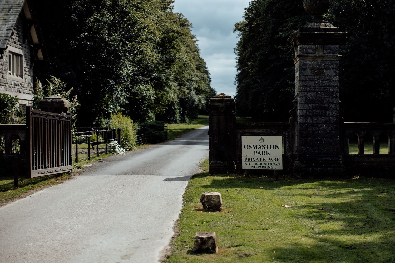 Tree-lined country road leading to a stone entrance gate.