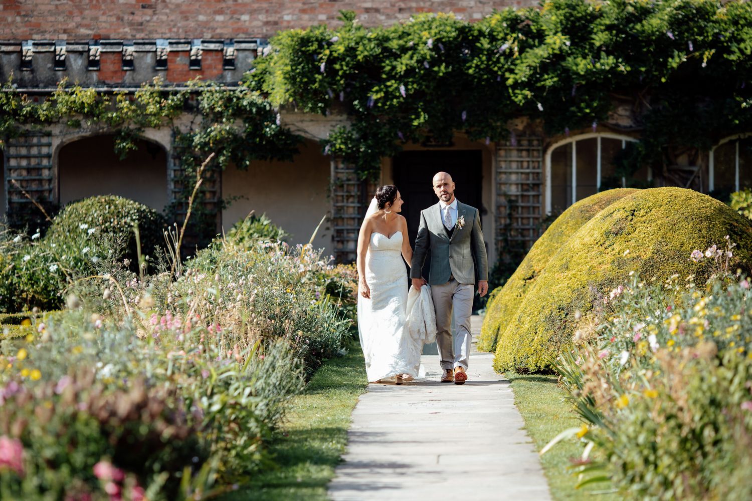 Garden pathway leading to wedding venue with blooming flowers and greenery.