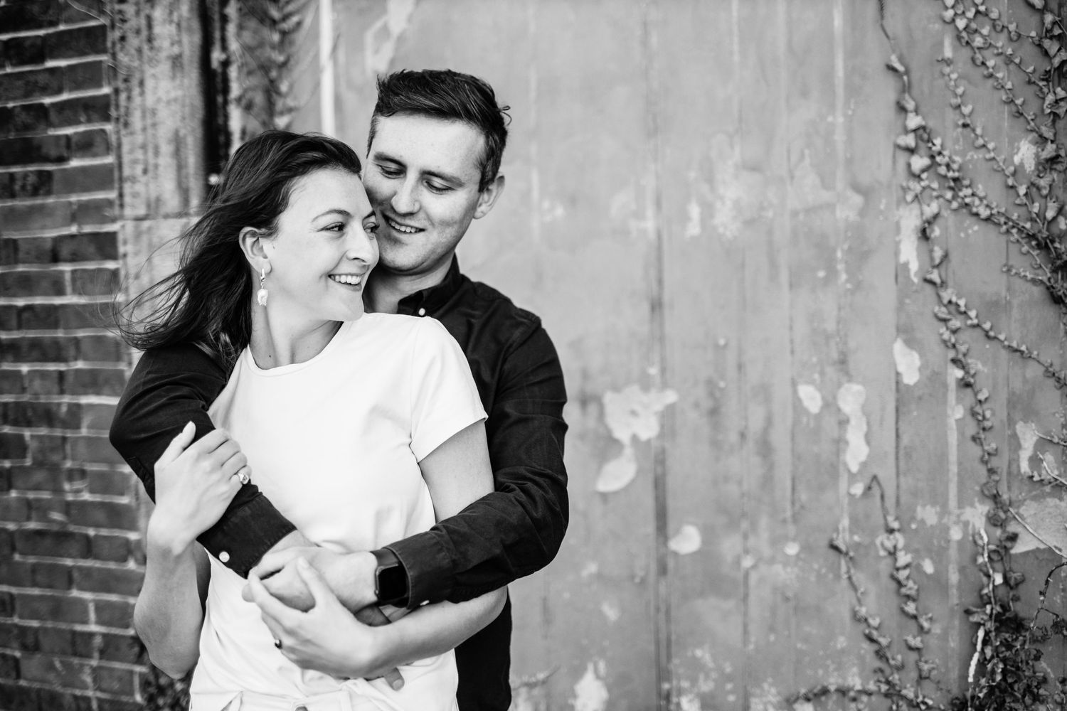 Couple embracing against rustic brick wall background in vintage style portraits.