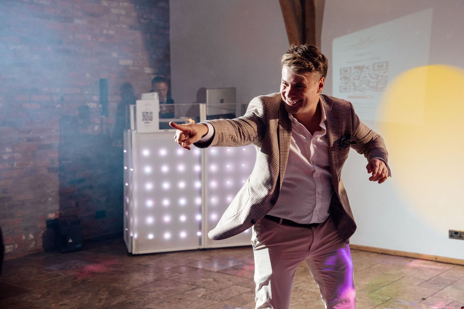 Energetic dancer in a brown suit moves on a dance floor with illuminated LED panels in the background.