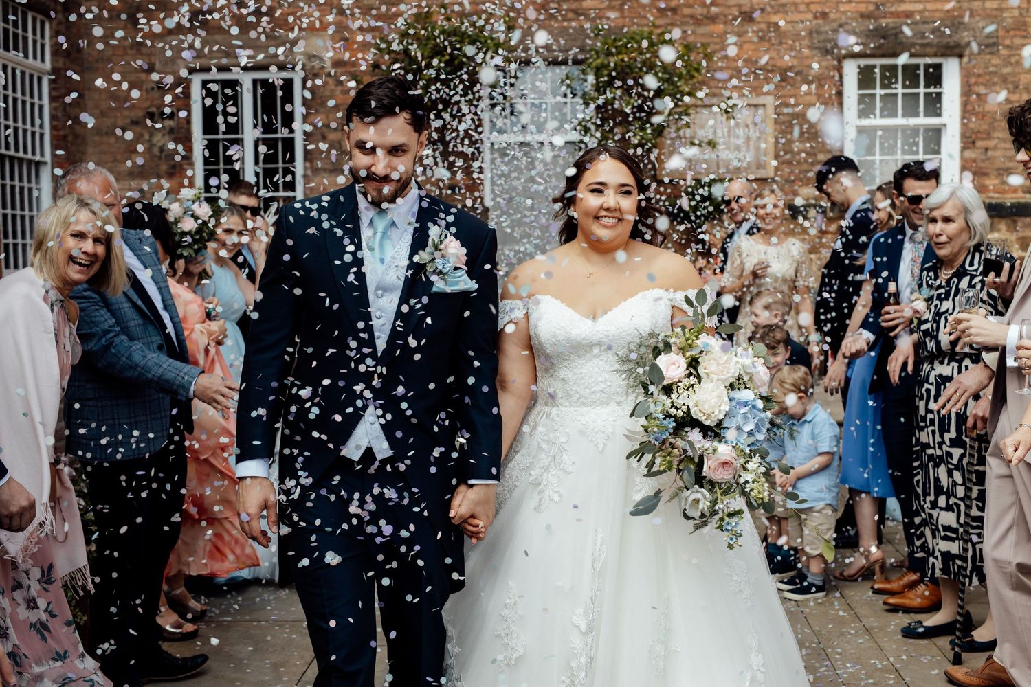 Guests throwing confetti at wedding celebration outside brick building.
