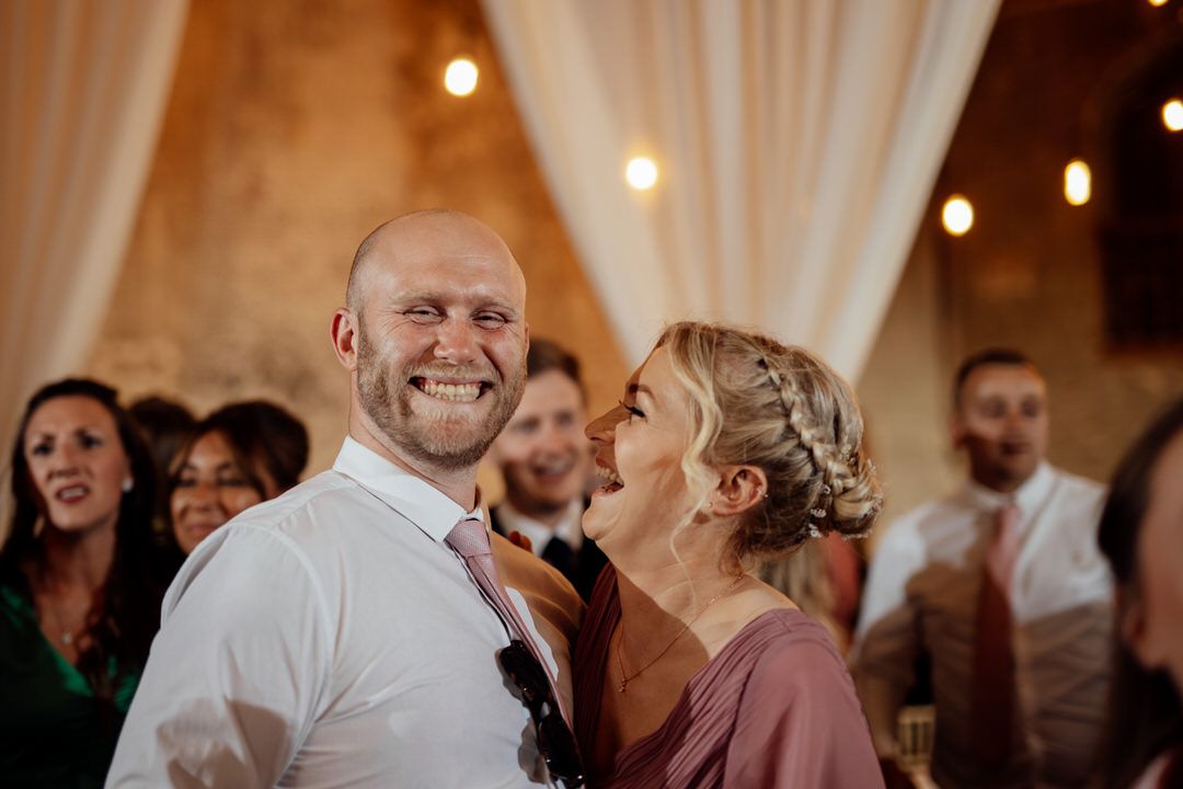 Wedding reception celebration with guests dancing under warm lighting.