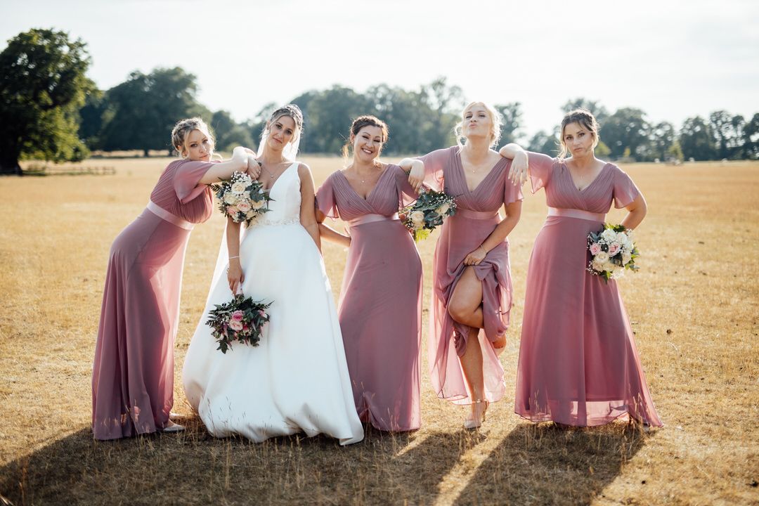 Bridal party in dusty rose dresses poses together in golden field during sunset.