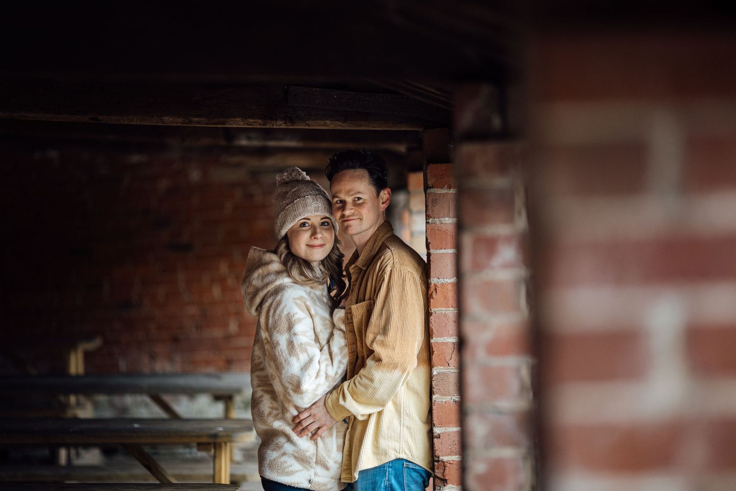 A couple embracing in a rustic setting with exposed brick walls.