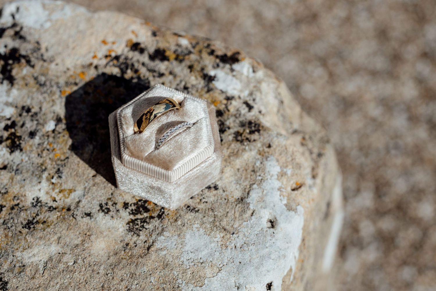 Close-up detail shot of wedding rings on a textured stone surface.
