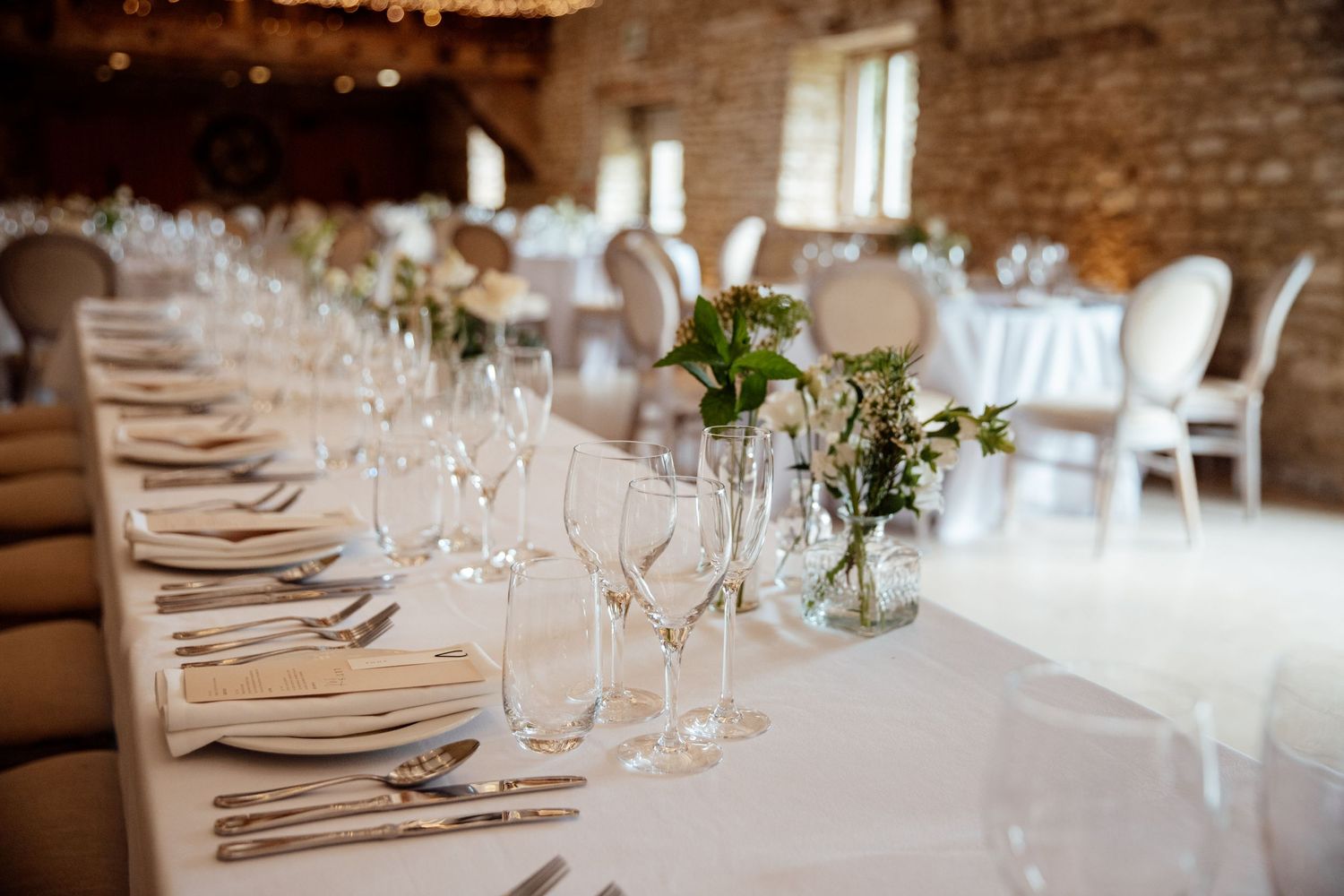 Elegant wedding reception table settings with glassware and floral centerpieces.