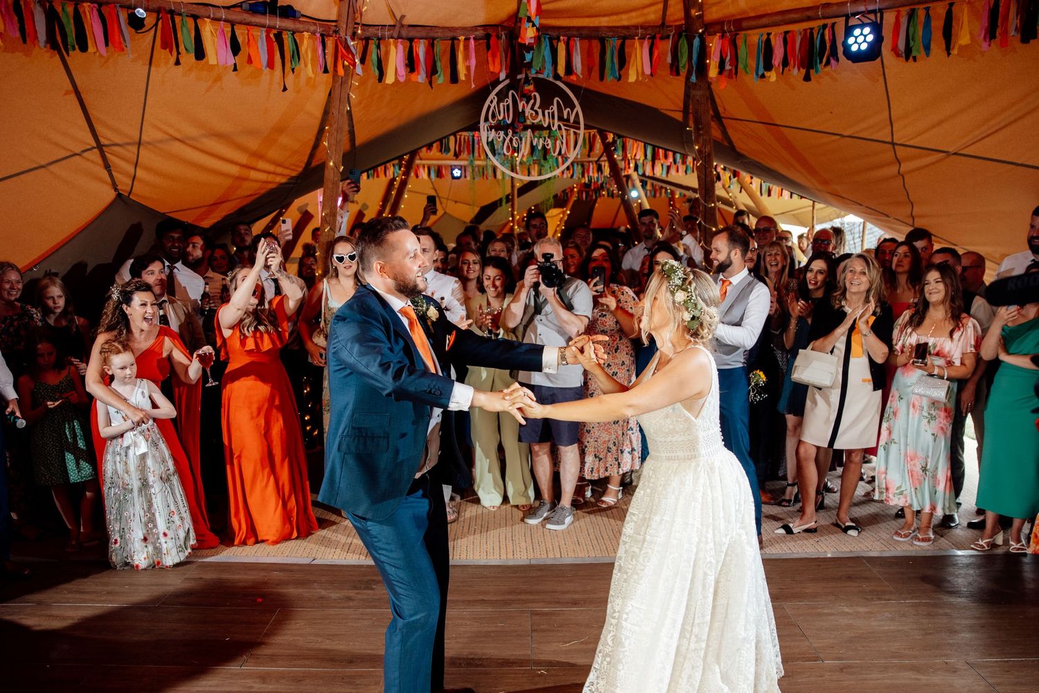 Couple dancing under festive bunting at wedding reception with guests watching.