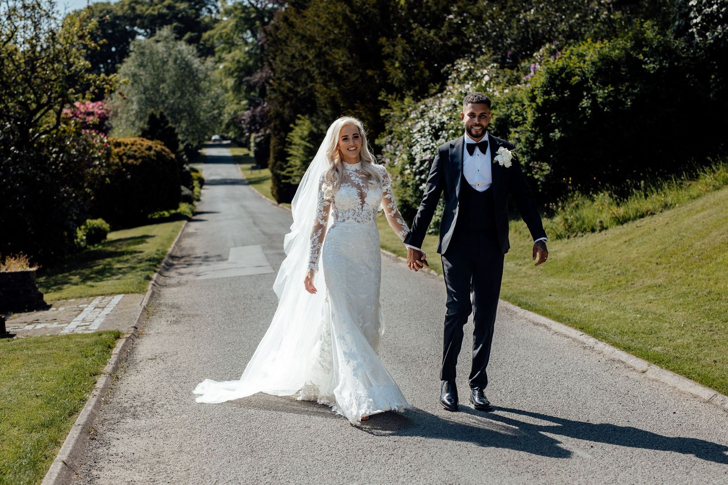 Couple walks along a tree-lined pathway in wedding attire.