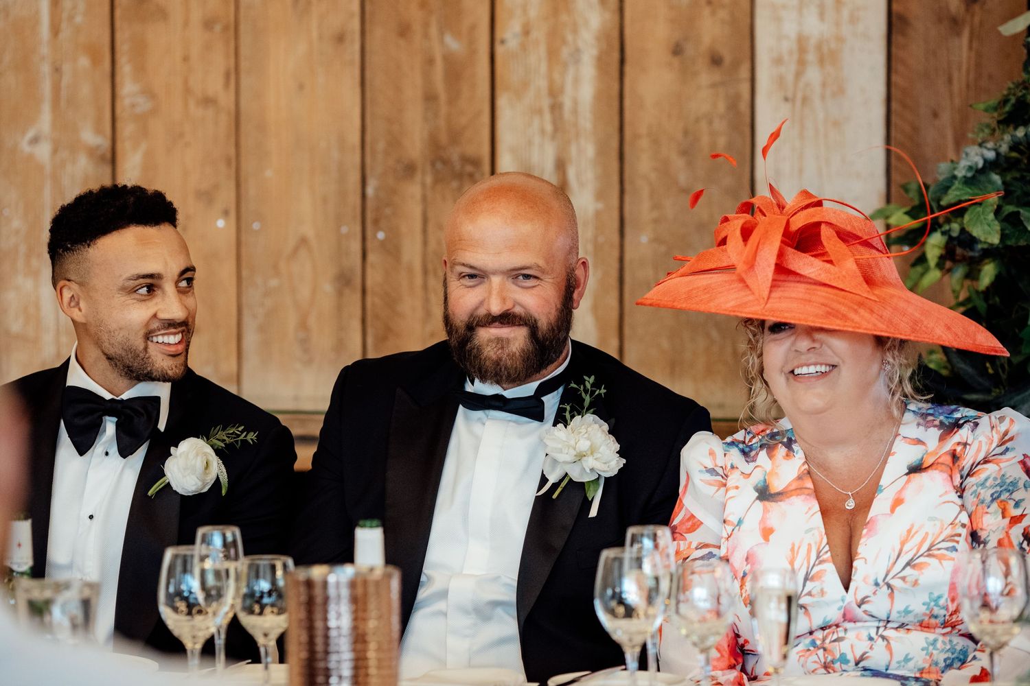 Wedding reception guests in formal attire seated at a rustic wooden table.