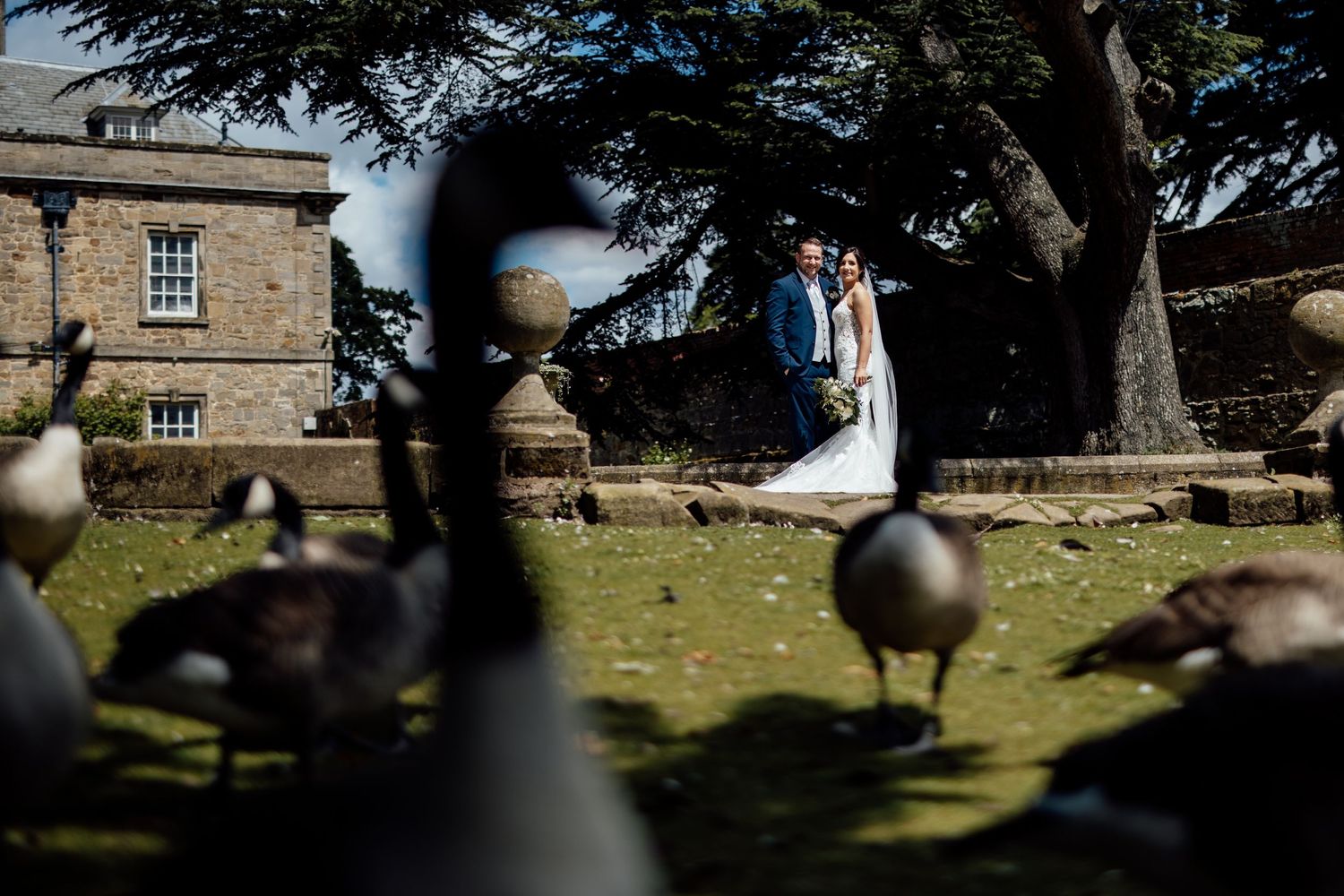 Stone buildings and trees create a scenic backdrop on a sunny wedding day.