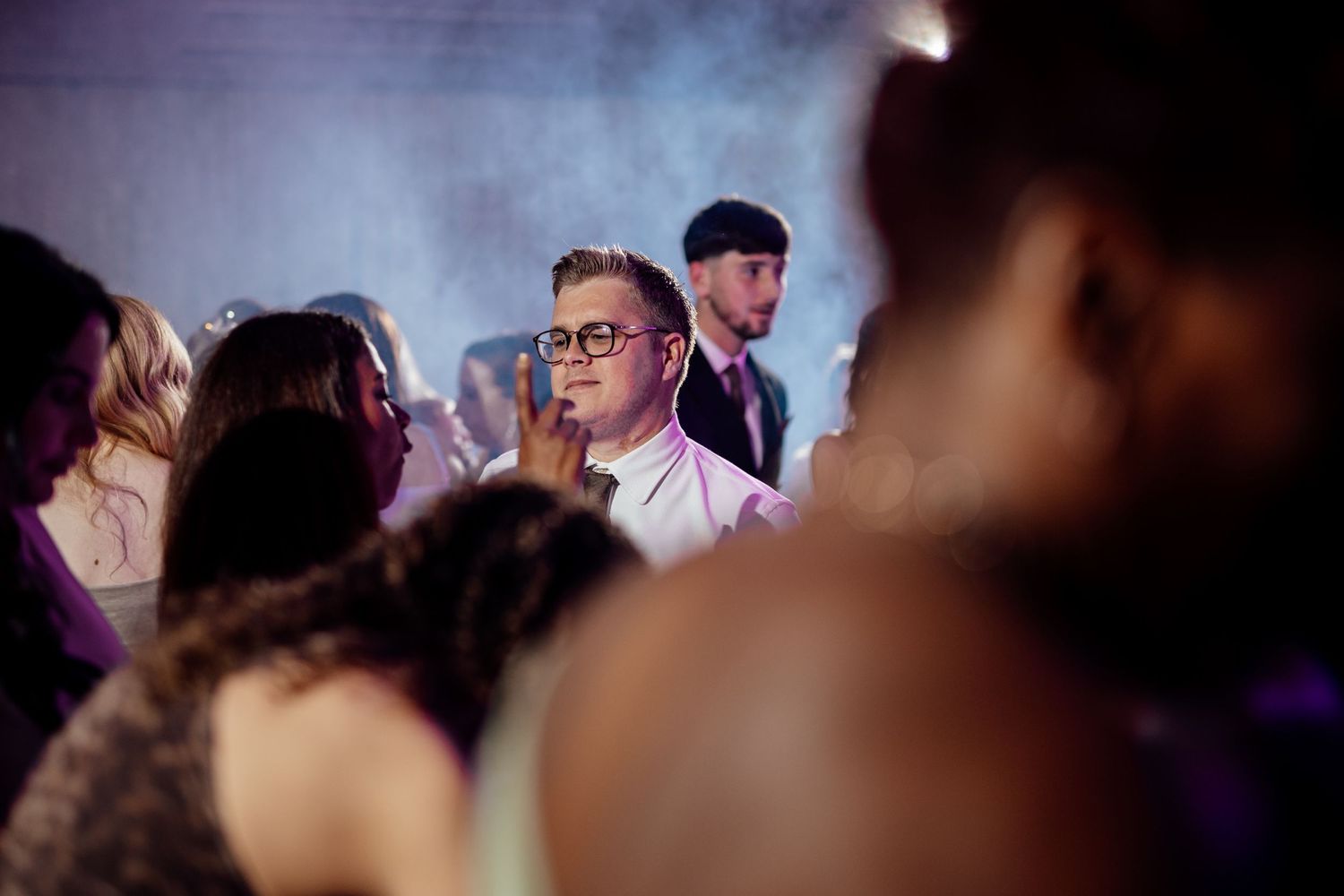 Guests enjoying a lively dance party at a wedding reception with atmospheric lighting and smoke effects.
