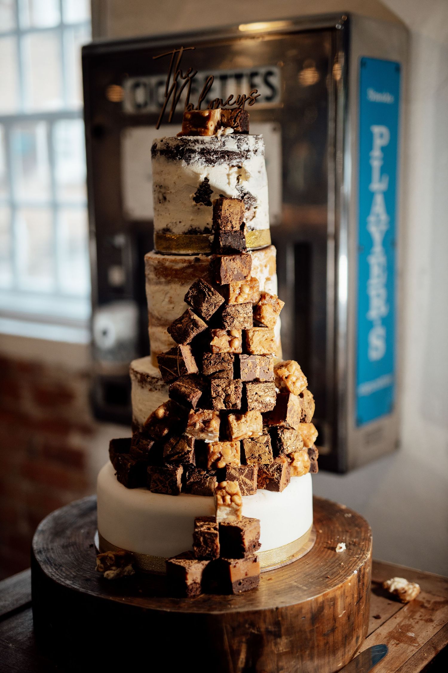A unique wedding cake decorated with stacked brownie squares on a wooden stand.