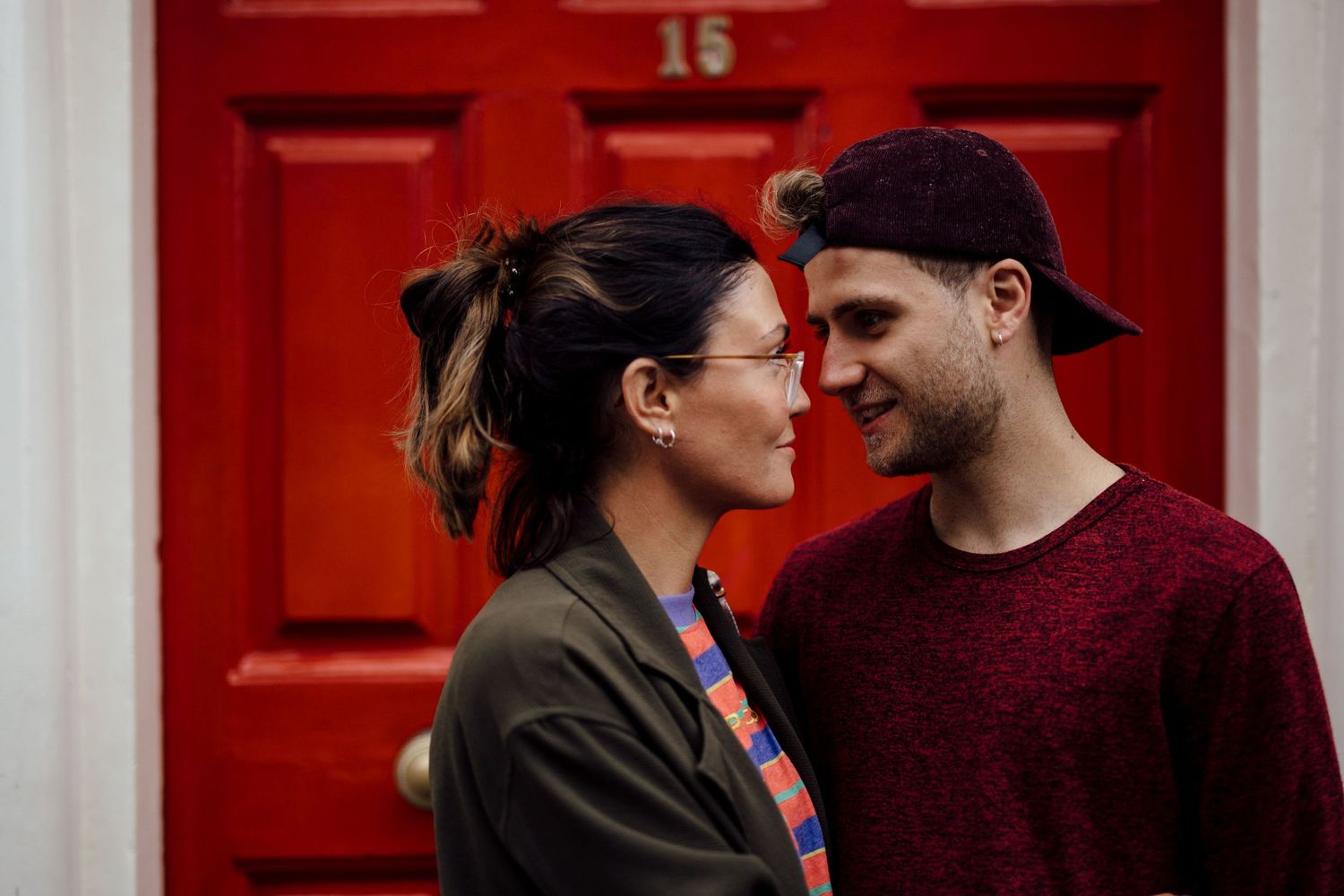 A couple shares an intimate moment in front of a bright red door.