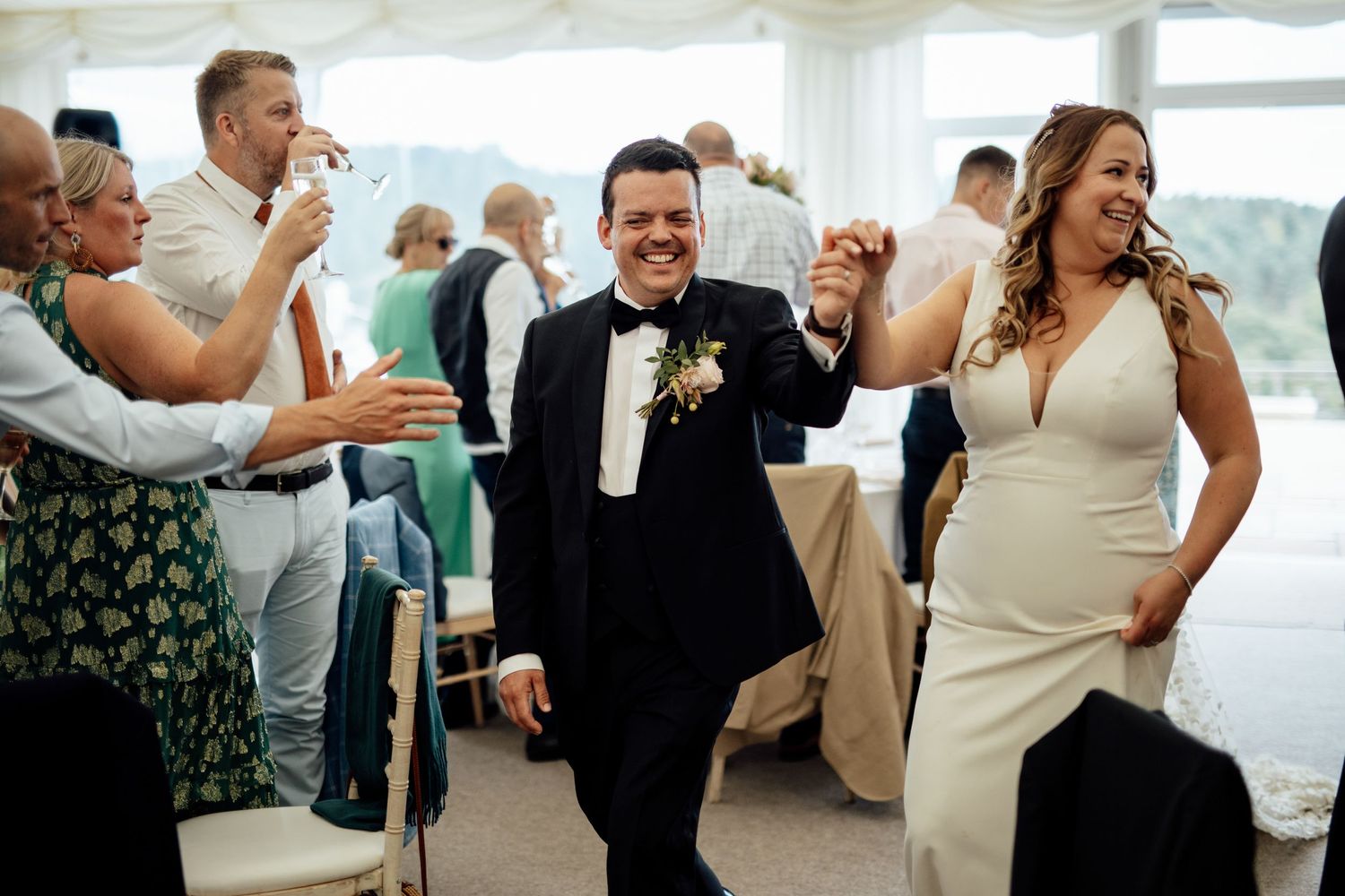 Wedding reception guests dancing and celebrating under white tent.