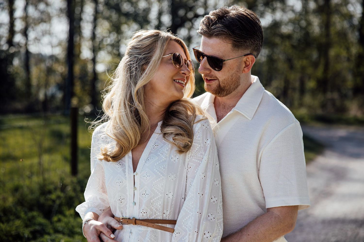 Couple sharing tender moments while walking on sunny forest path.