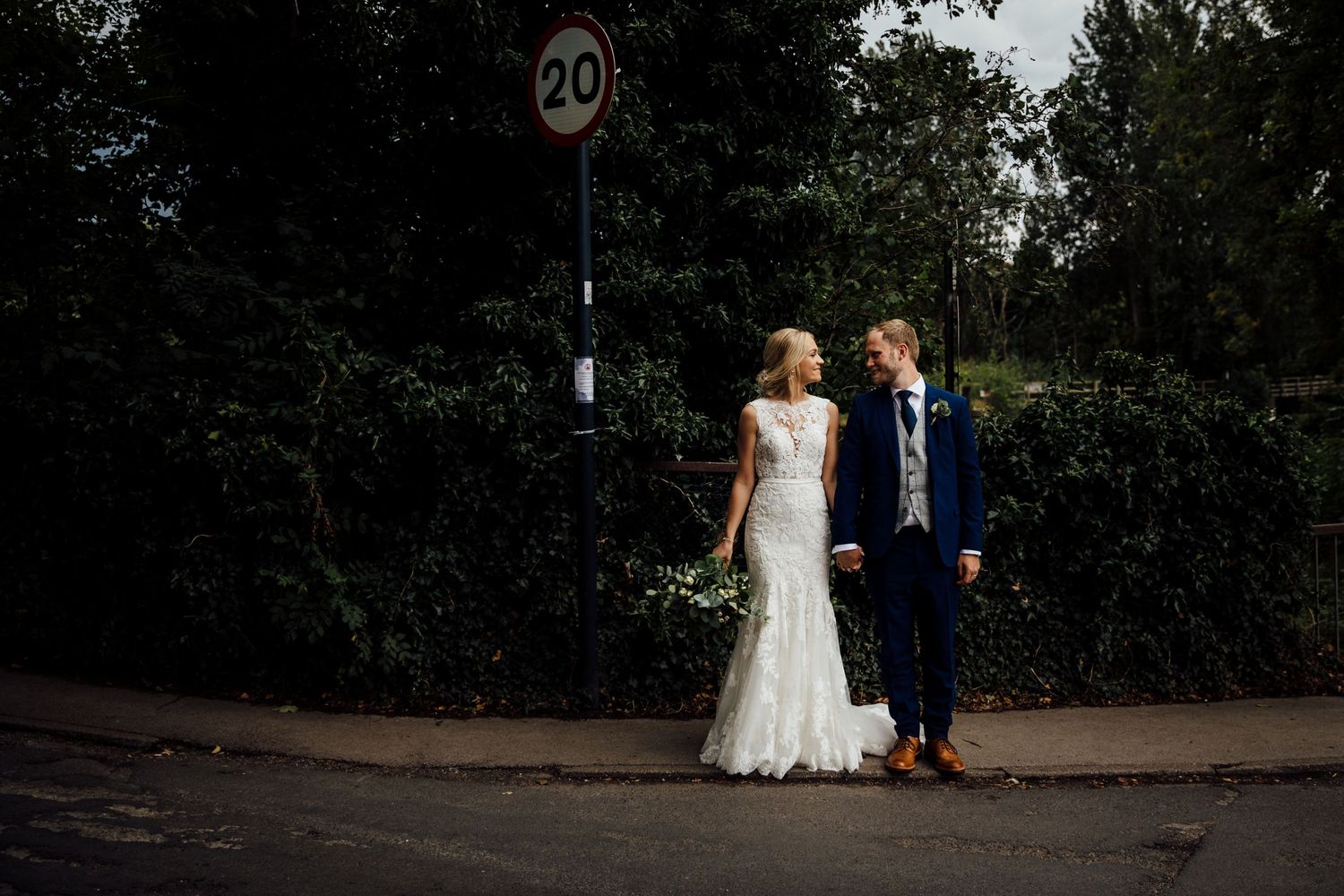 Wedding couple walking together outdoors on a stone path surrounded by greenery.