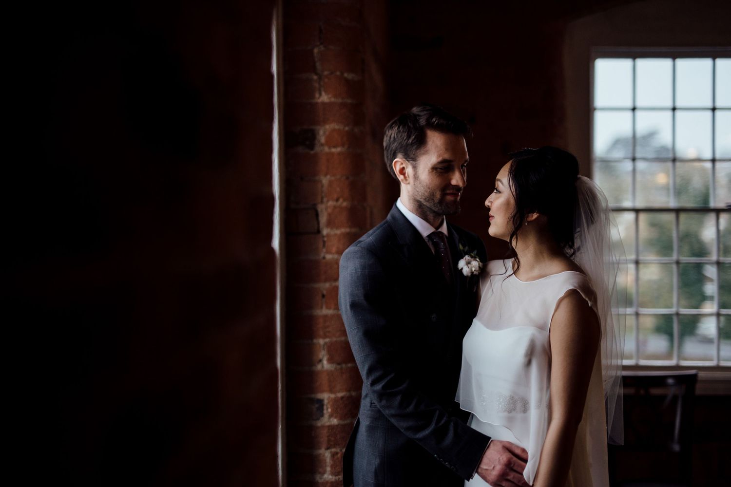Romantic silhouette of couple against window light in brick-walled room.