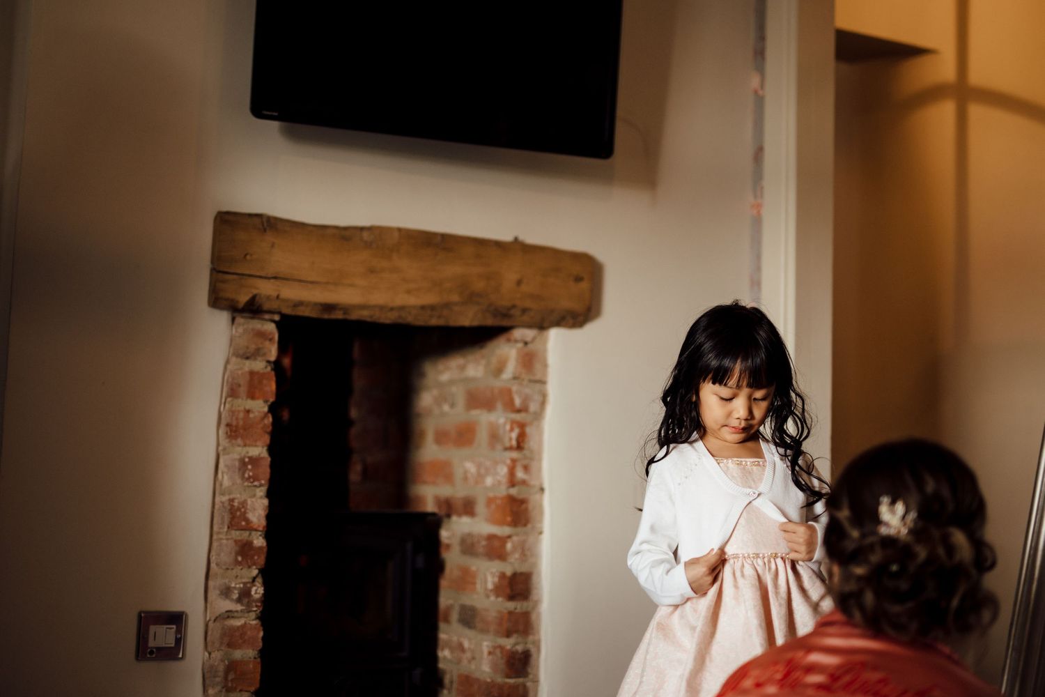 Young girl in white dress preparing for ceremony in rustic brick room.