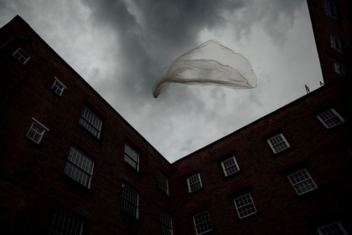 Dramatic upward view of brick building facade under stormy skies.