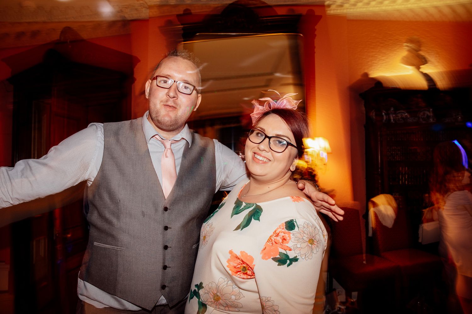Wedding reception guests dancing and celebrating in warm orange-lit venue.
