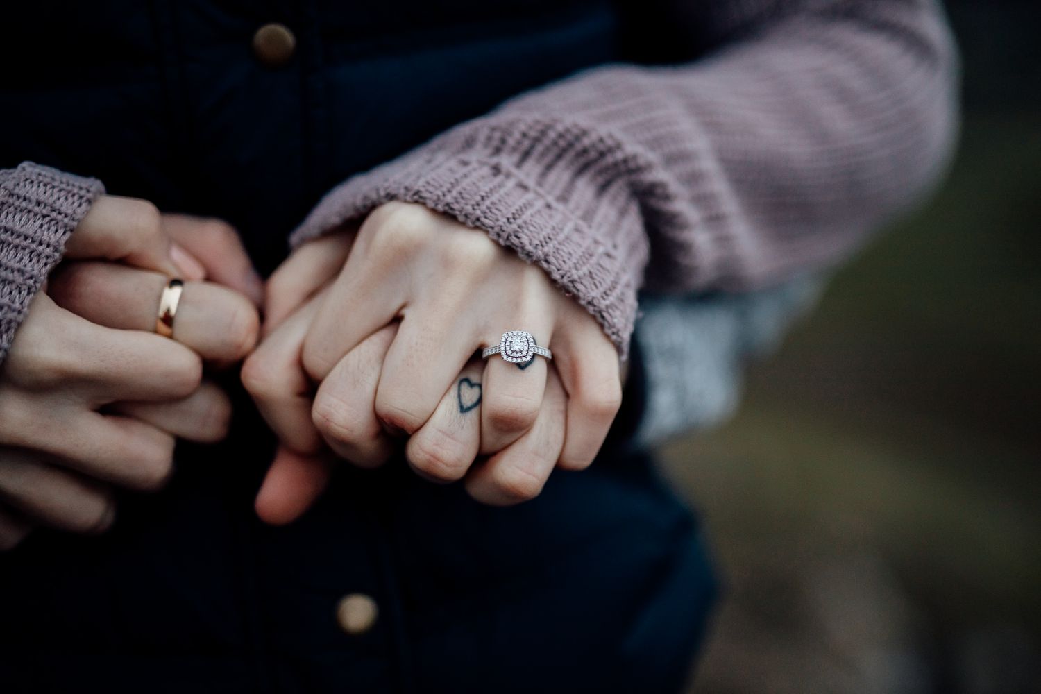 Close-up of intertwined hands wearing engagement rings and cozy knit sweaters.
