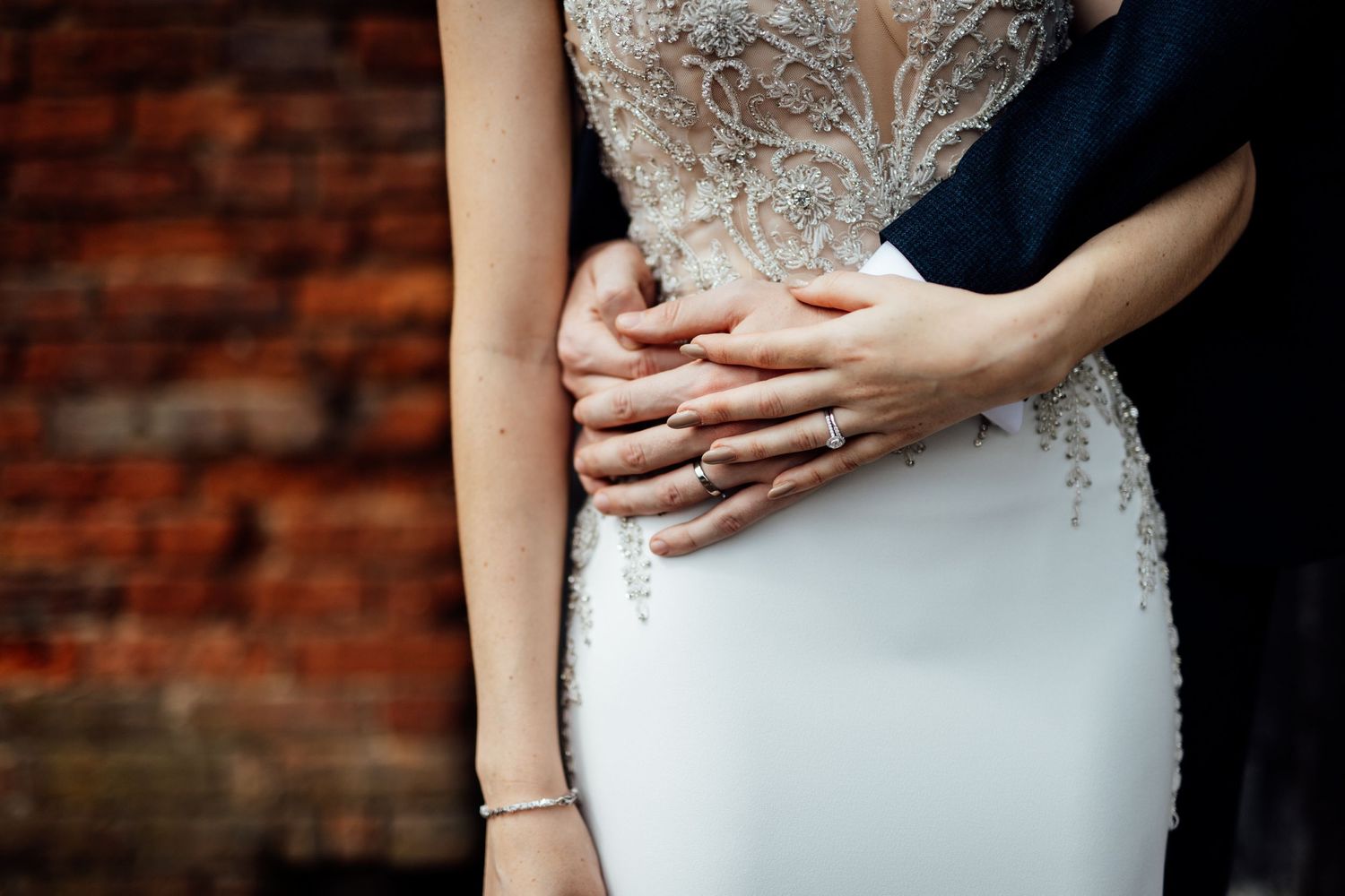 Close-up detail of an elegant lace wedding dress against brick wall backdrop.
