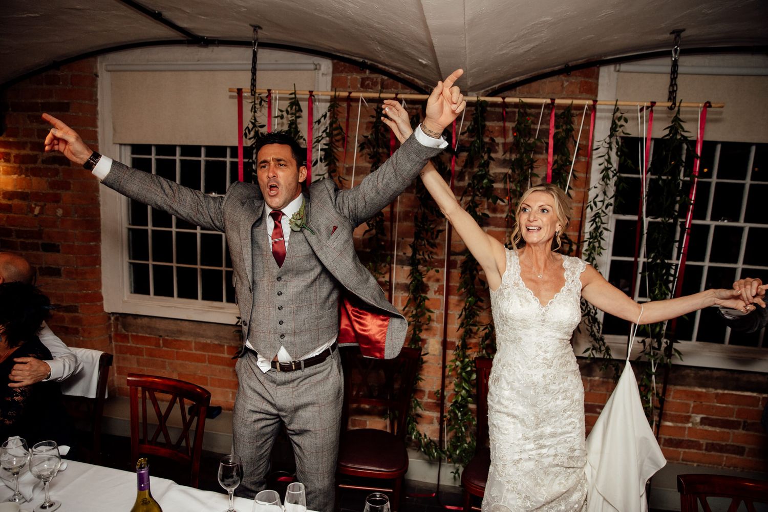 Newlyweds celebrate with joyful arms raised during their wedding reception in a rustic venue.