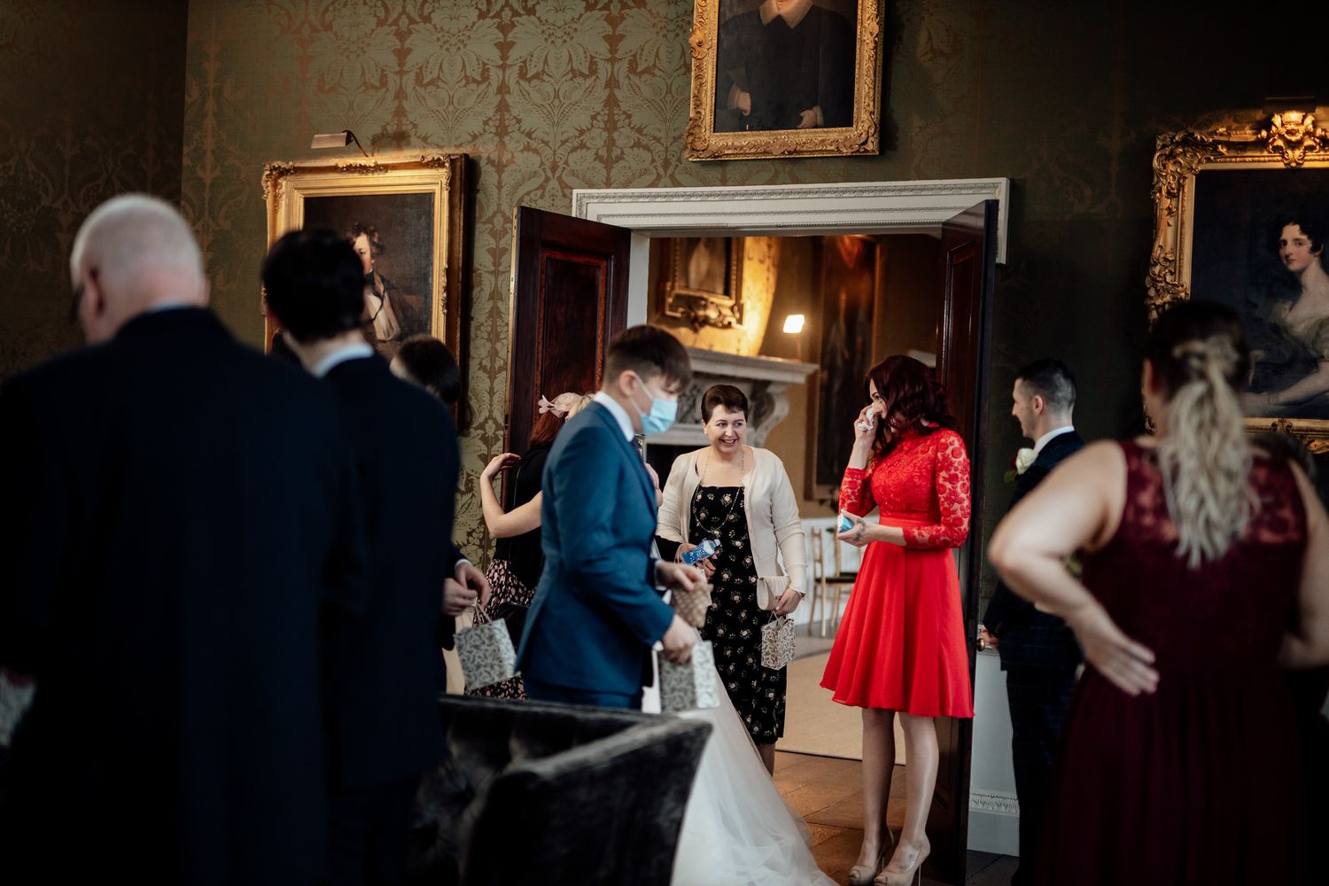 Wedding guests mingling in an ornate room with vintage decor and a warm atmosphere.