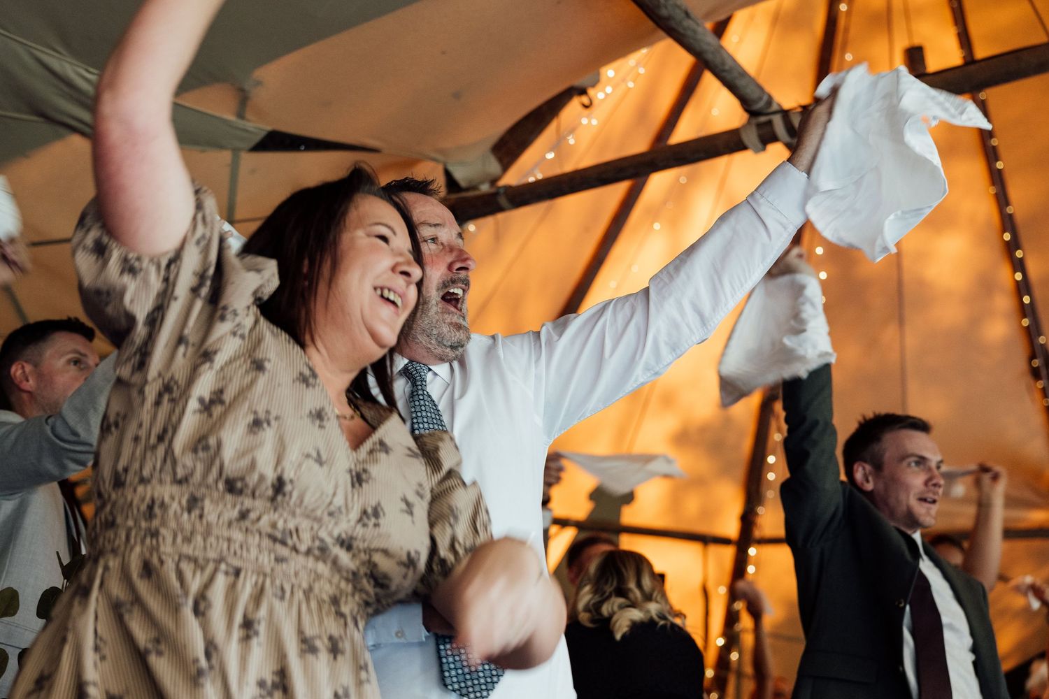 Joyful wedding reception celebration with dancing under warm ambient lighting.