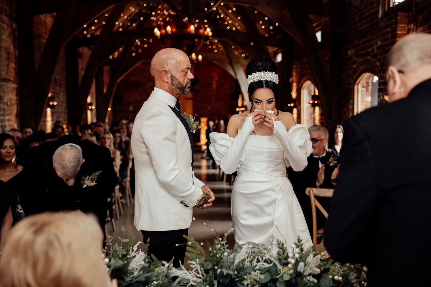 Wedding guests celebrate on the dance floor under romantic string lights and chandeliers.