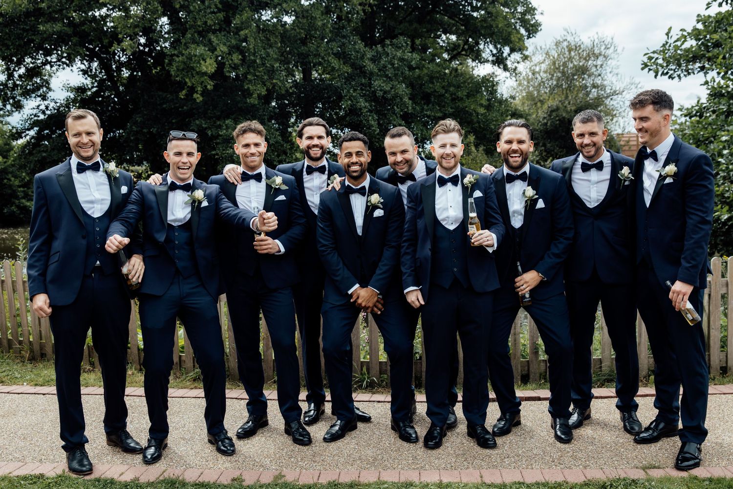 Groomsmen in navy suits show off their socks while sitting on a wooden fence.