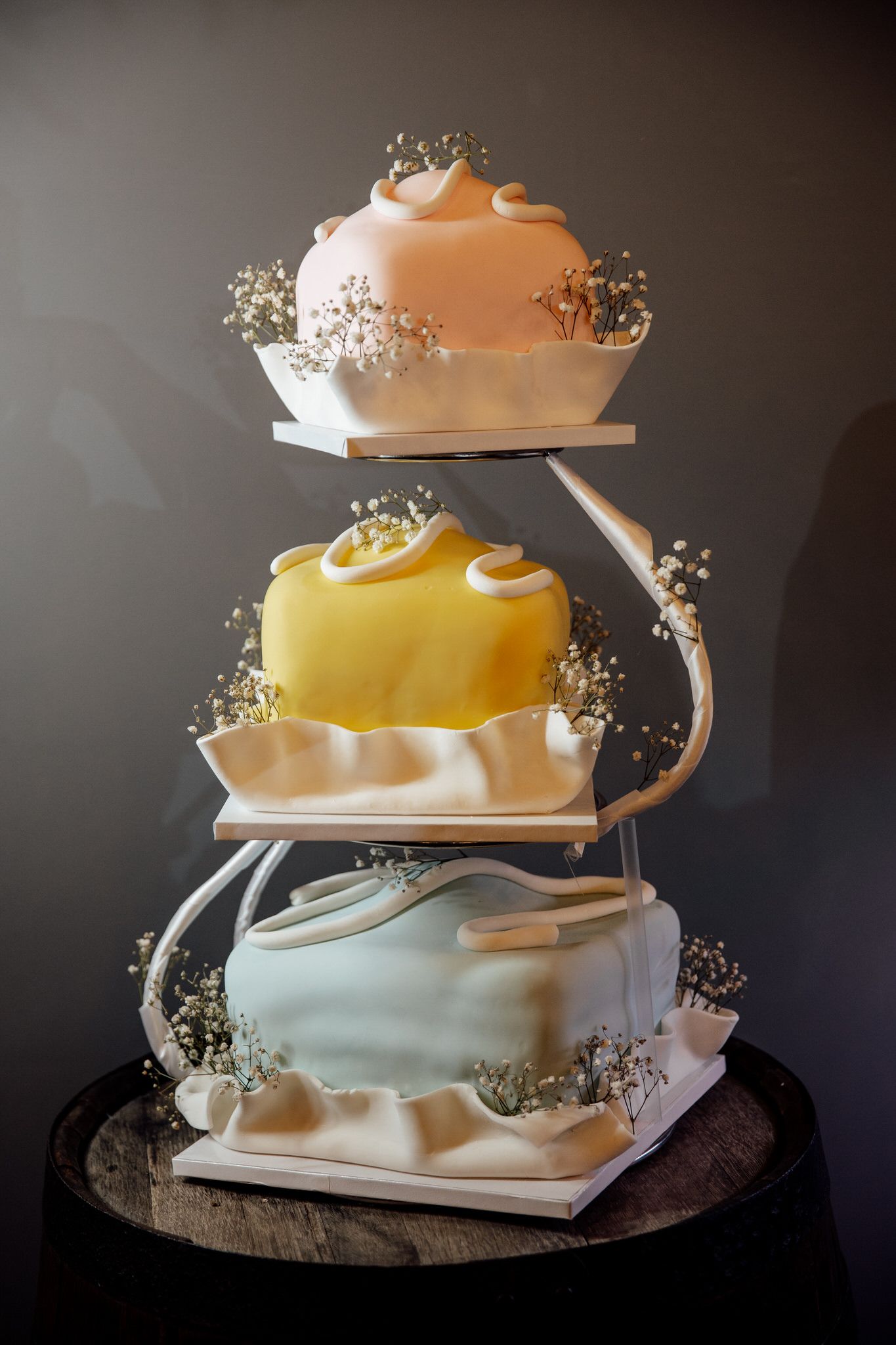 Modern abstract wedding cake with flowing tiers in white and yellow decorated with baby's breath flowers.